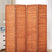 4-panel saddle brown room divider made of wood and bamboo, displayed in a cozy bedroom setting next to a white dresser and lamp, providing functional privacy.