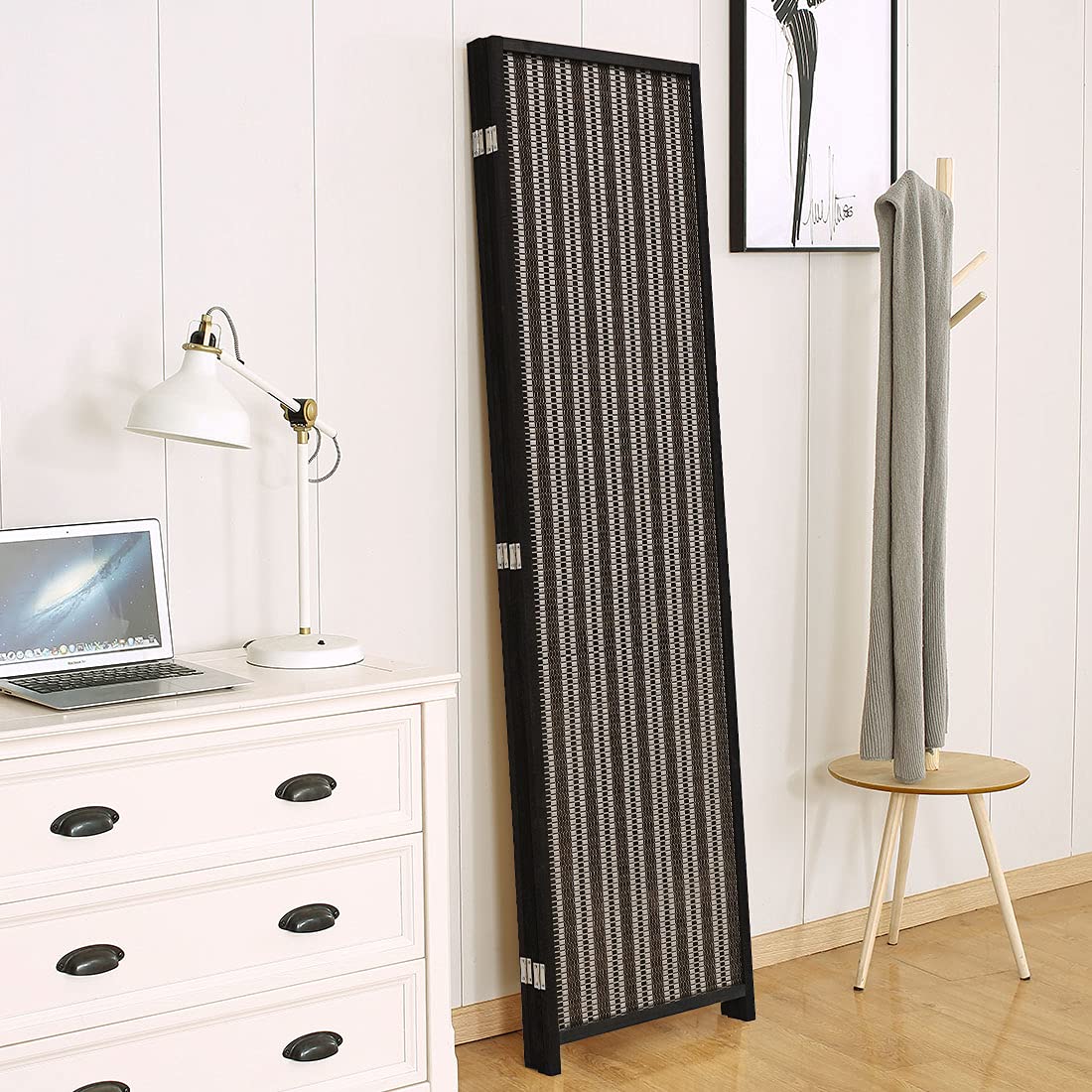 Folded black 4-panel room divider stored compactly beside a white dresser and lamp, showcasing its space-saving and practical design for storage.