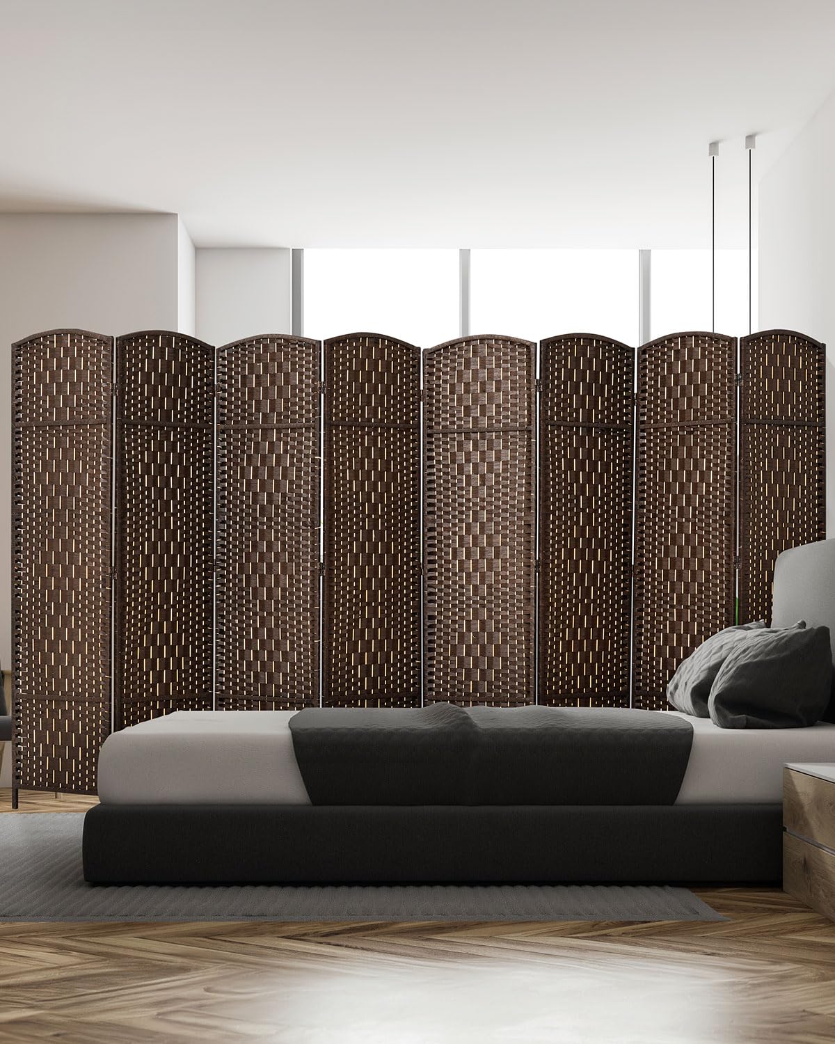An 8-panel dark brown bamboo room divider with a woven design stands behind a modern bed, blending style and privacy in a bright, minimalistic bedroom.
