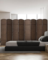 An 8-panel dark brown bamboo room divider with a woven design stands behind a modern bed, blending style and privacy in a bright, minimalistic bedroom.