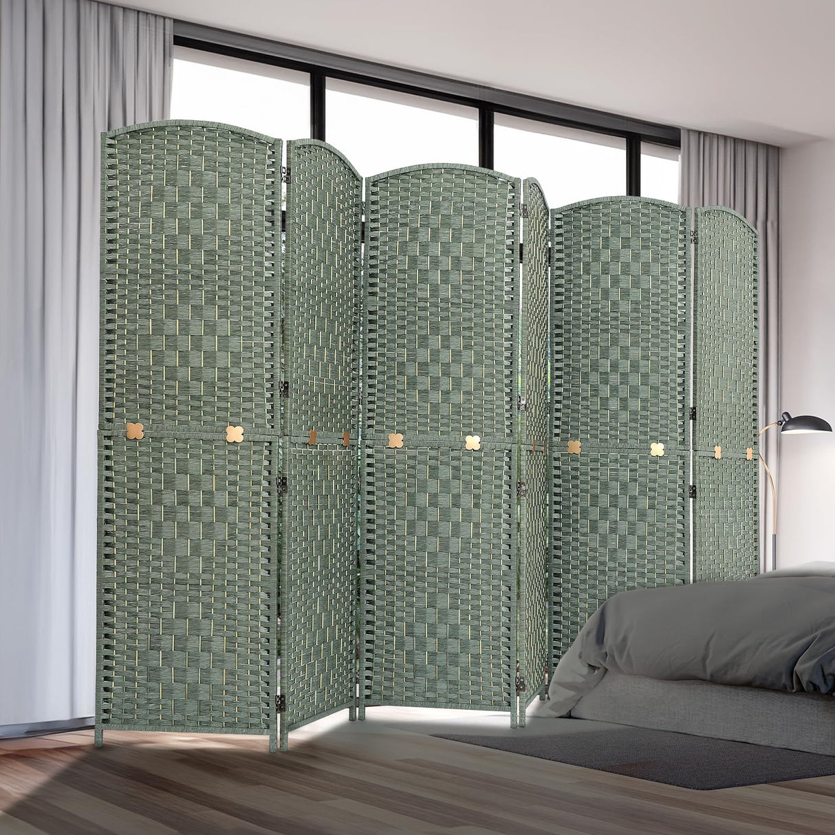Room divider with six woven panels in natural bamboo and wood, displayed in a bedroom setting near a bed and curtains, offering privacy and style in a green finish.